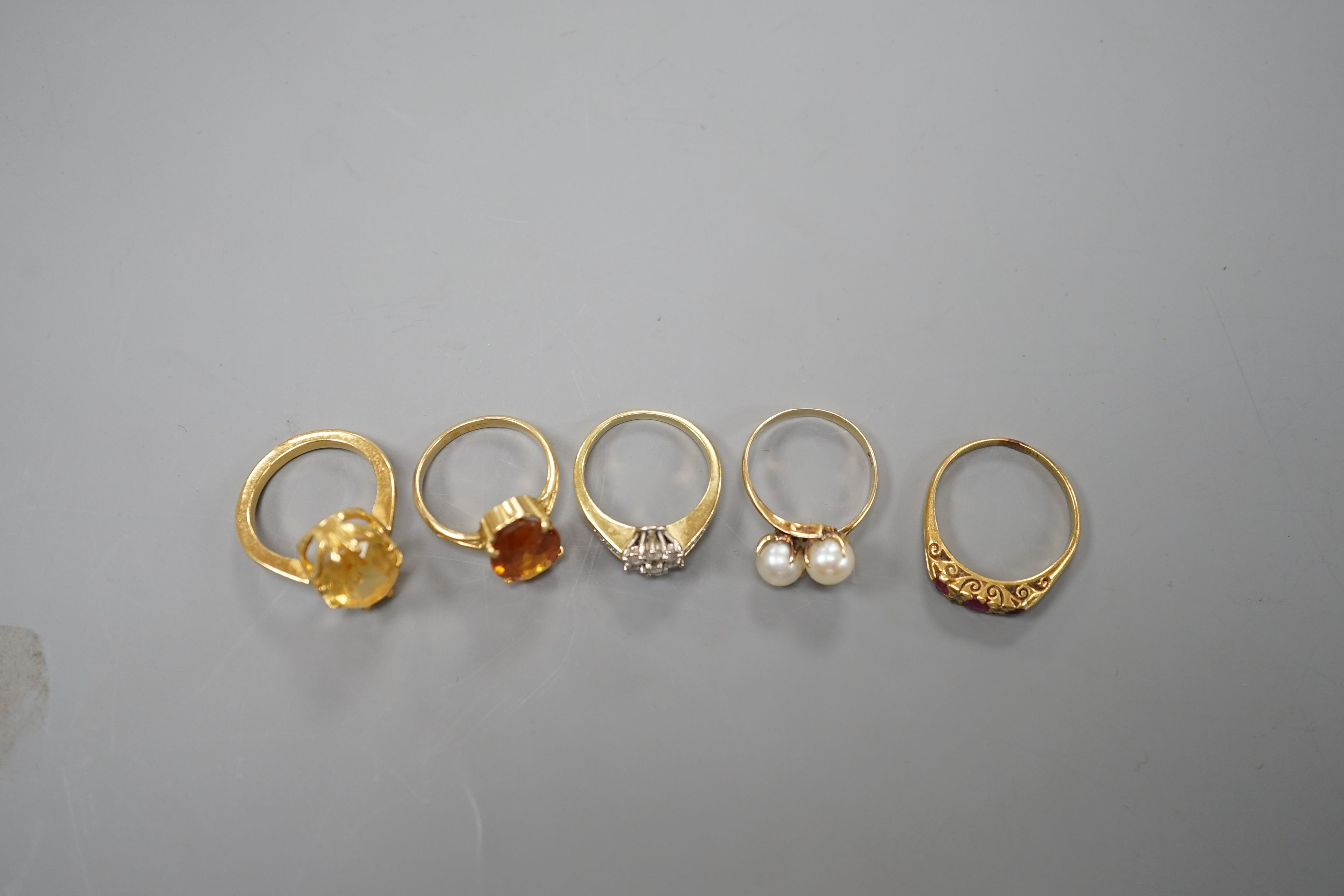 Five assorted gold and gold coloured metal dress rings, comprising a two stone cultured pearl stamped 18k, size L, an 18ct gold diamond cluster, size L, an unmarked citrine?, an 18ct orange stone, size L and an early 20t